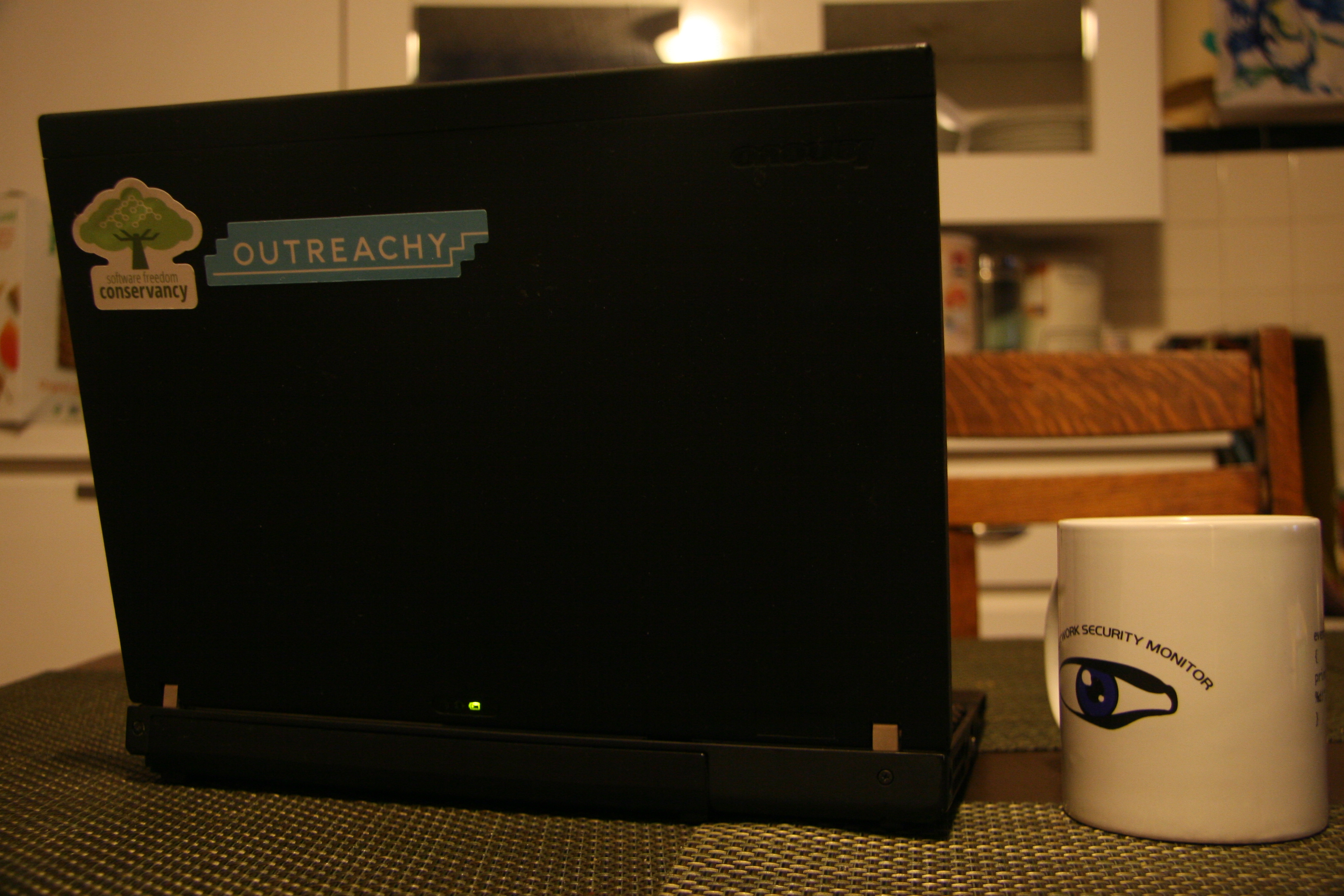A laptop with Conservancy and Outreachy stickers, alongside a Bro mug