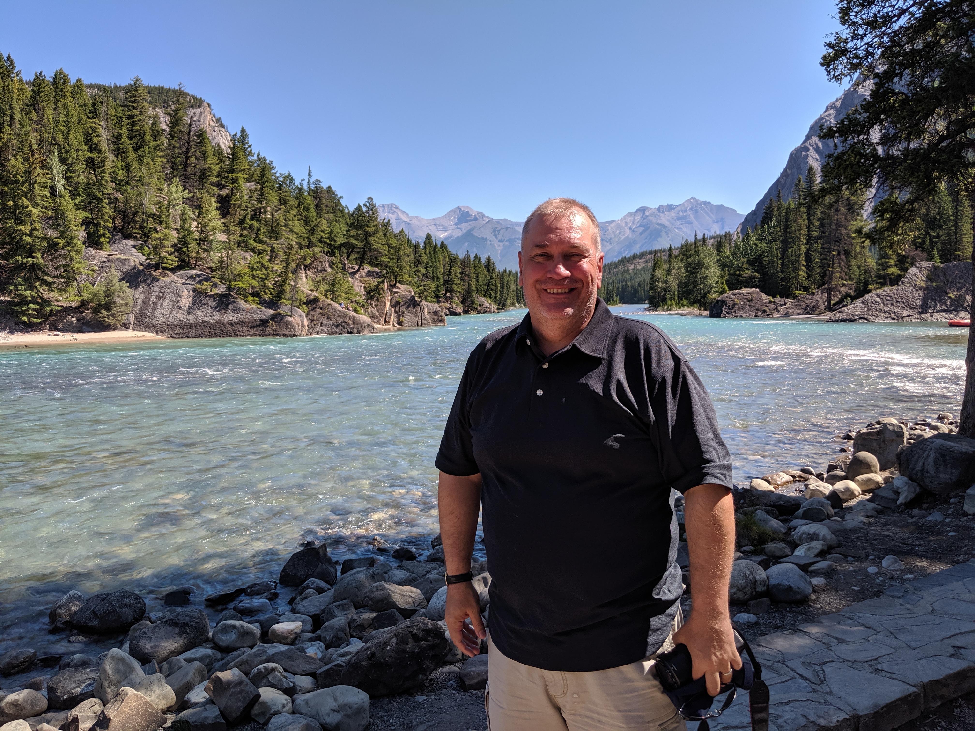 picture of Jeremy Allison in front of a beautiful nature landscape with water, mountains and trees.